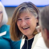 Woman smiling while looking and talking with gentleman seated at her table